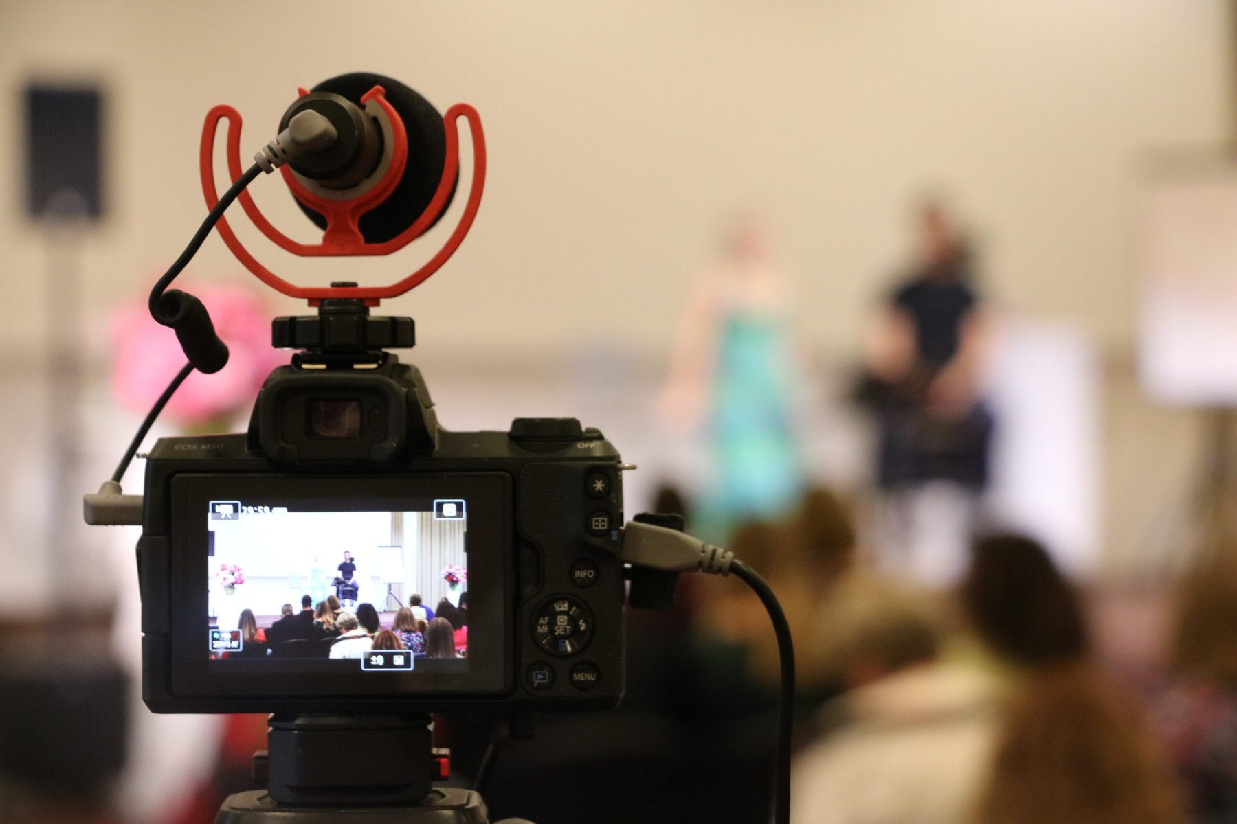 Caméra hybride professionnelle équipée d'un microphone filmant une cérémonie en direct, le public assis visible sur l'écran de la camérarémonie dans une salle